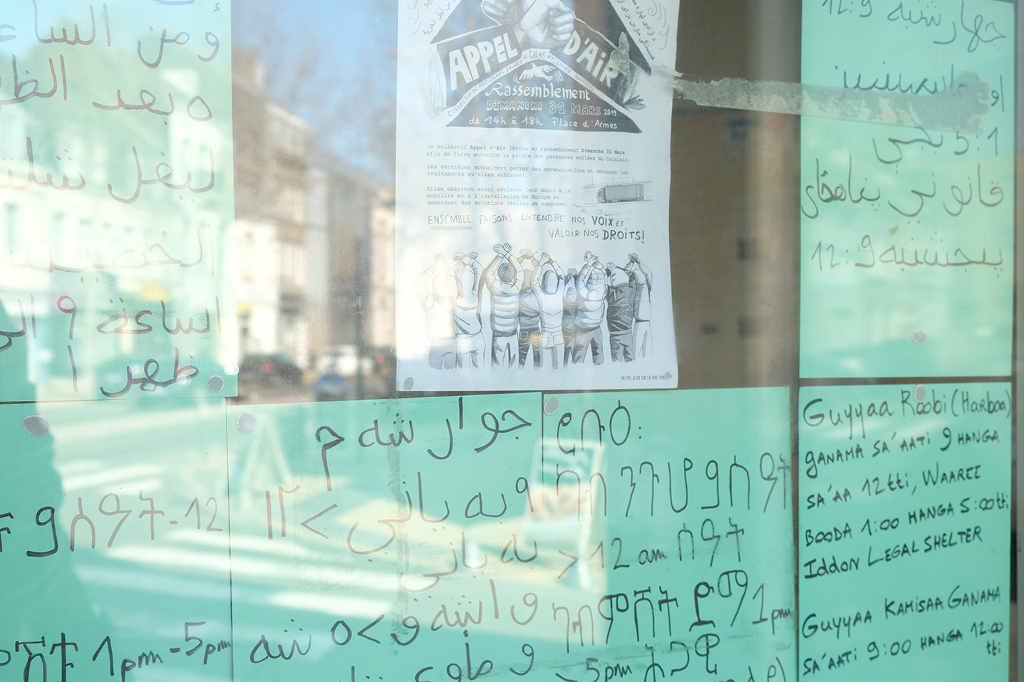 A l’entrée du local, l’affiche annonce la manifestation de dimanche 31 mars, encerclée par des feuilles où des explications sont inscrites dans différentes langues parlées par les exilés.