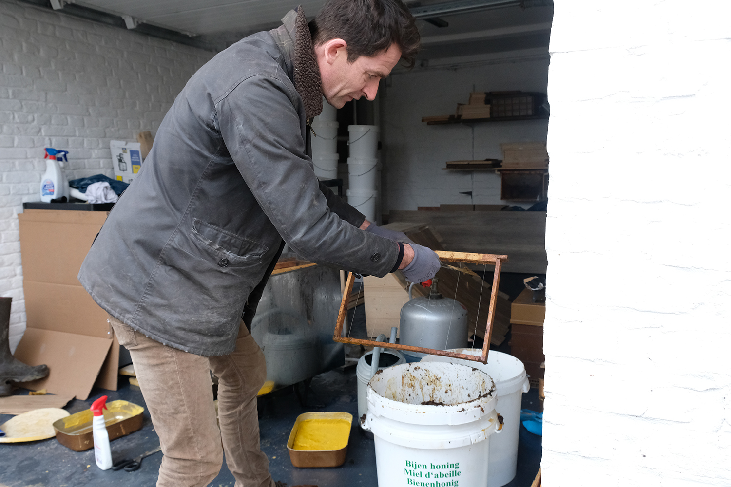 Sylvain TOUSSAINT est en train de gratter la cire d’abeille présente sur les cadres de ses ruches.